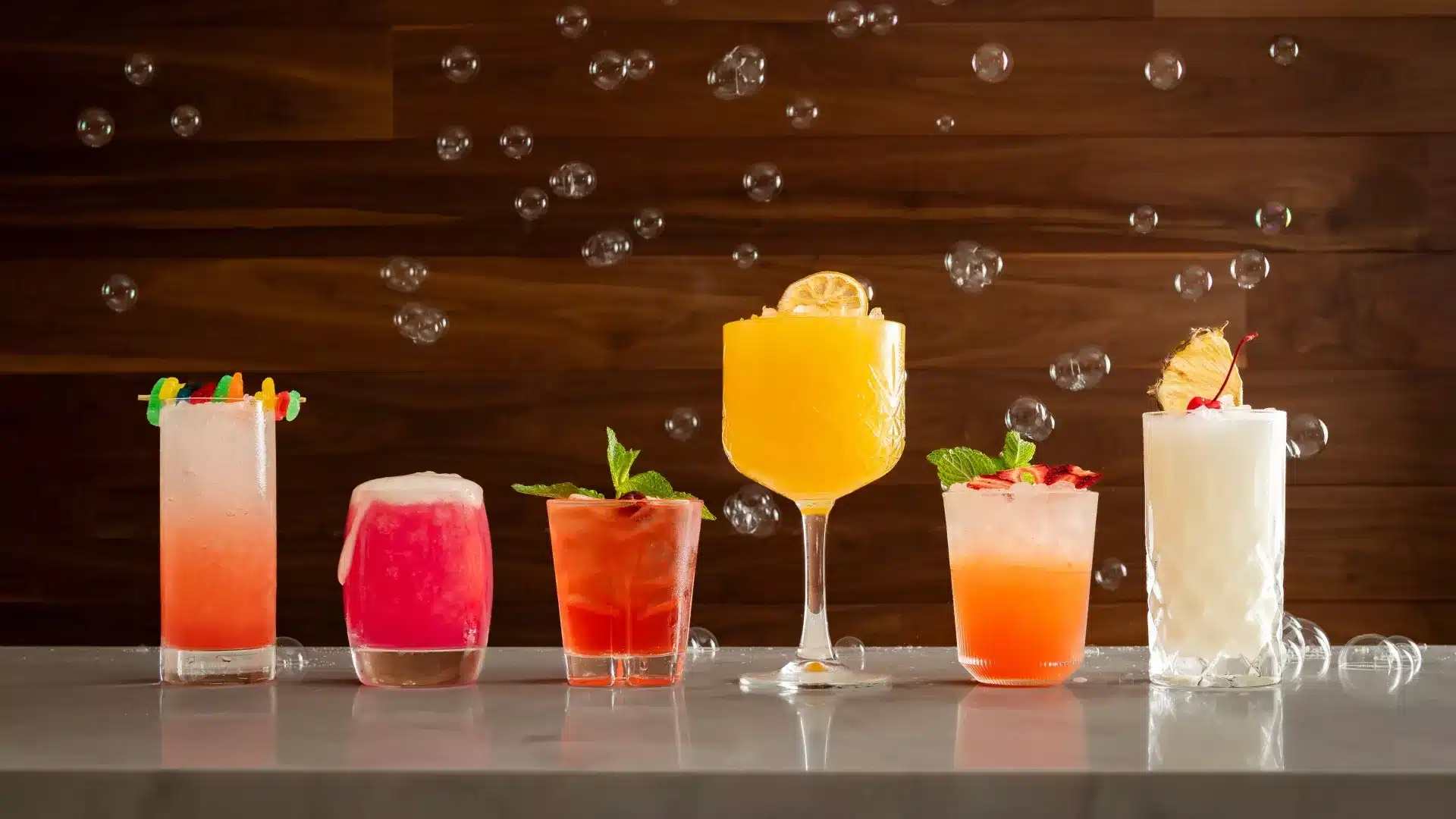 Six different colorful beverages on a bar.