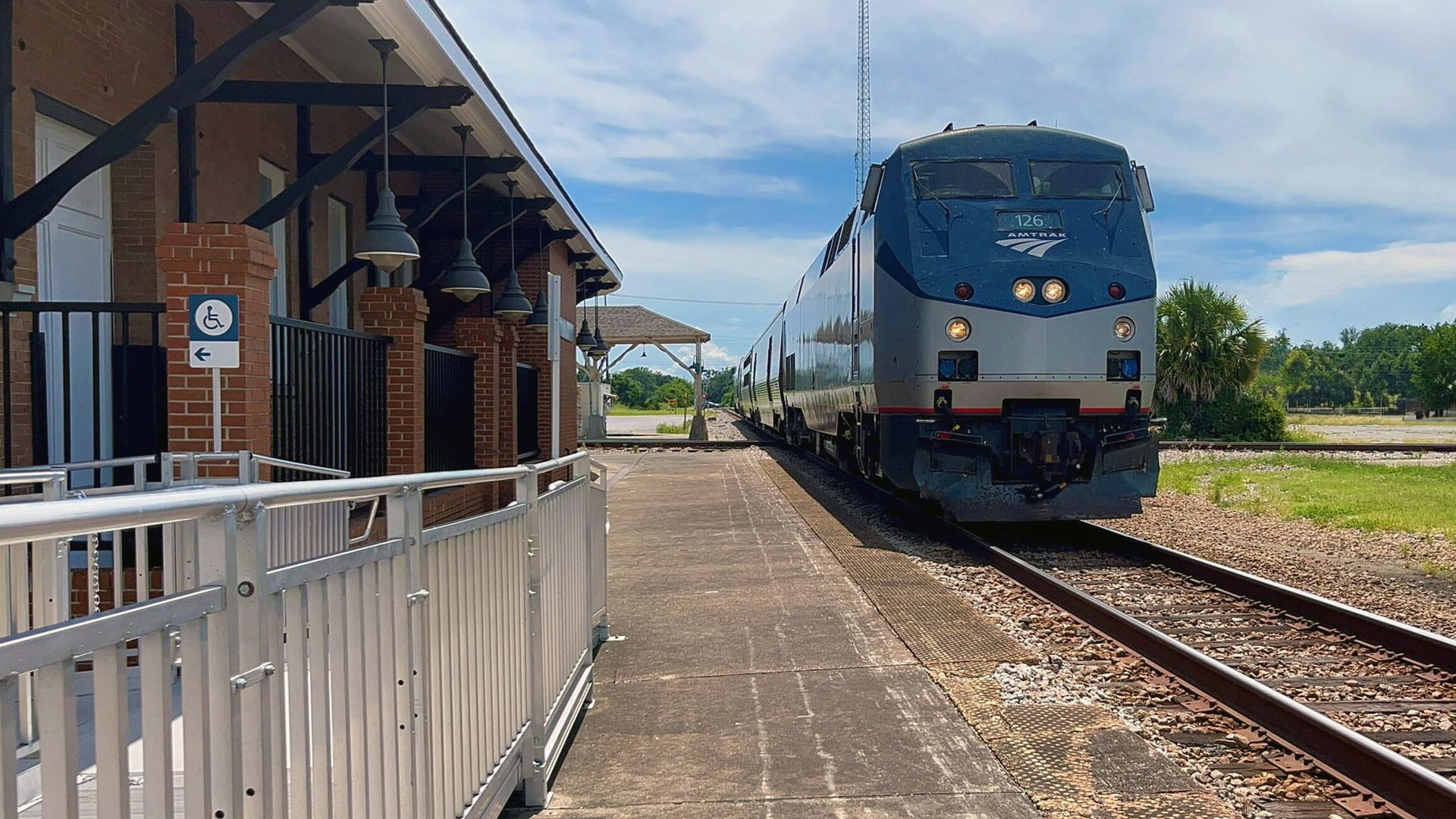 Blue and silver Amtrak train pulls into older brick station.