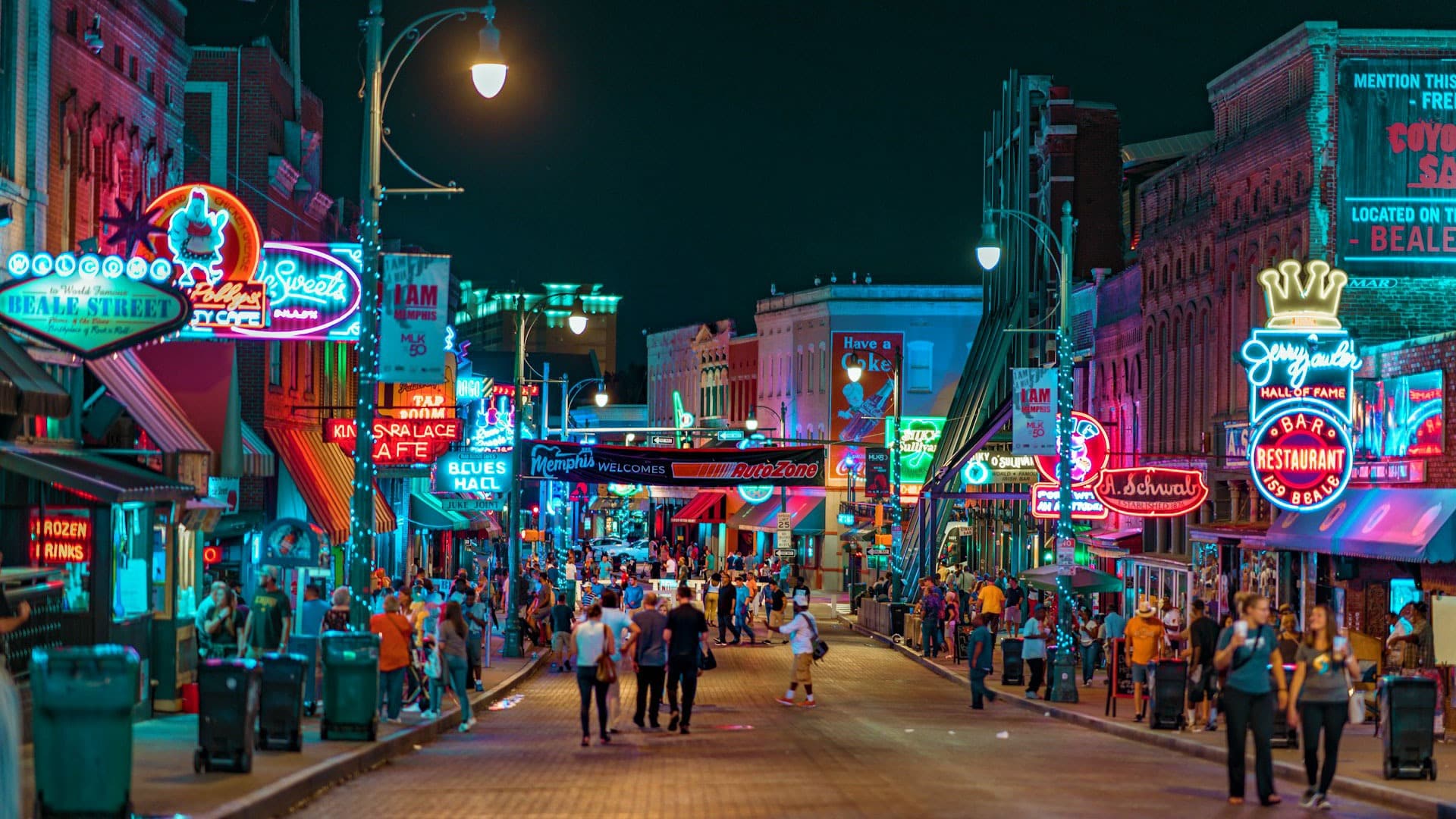 People walking down Beale Street in Memphis with neon lights of all colors on various brick buildings.