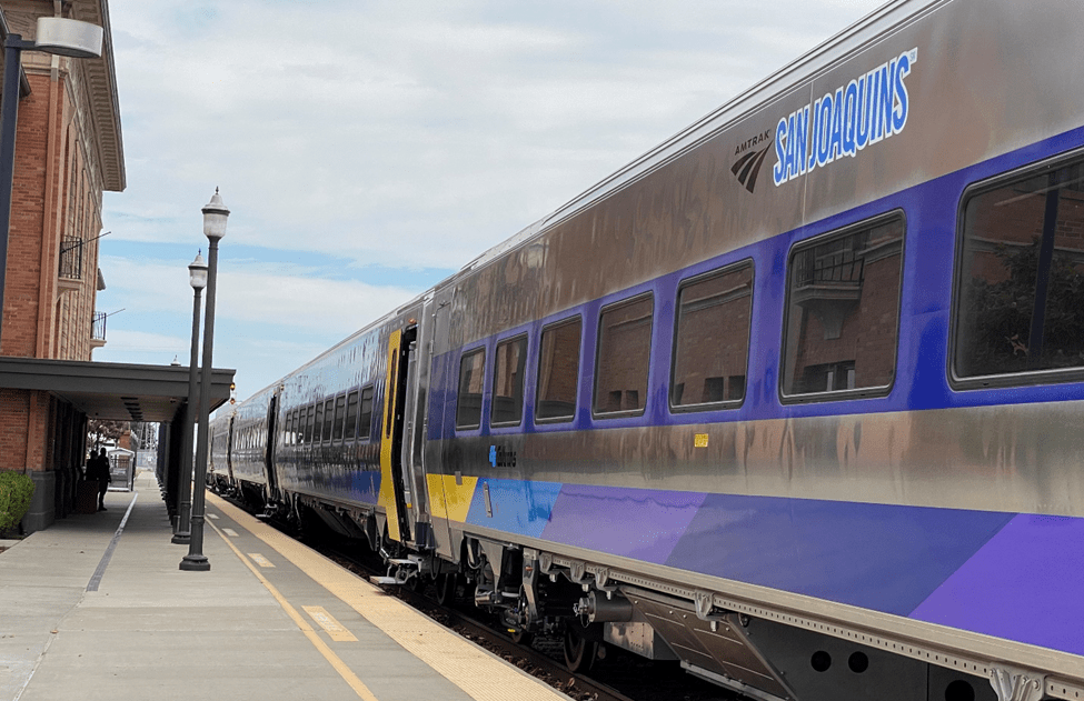 Silver passenger train with blue and purple stripe along the bottom edge.