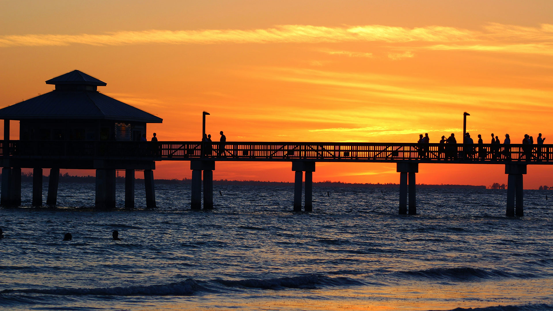 Silhouette of a pier at the beach with the sun setting behind.