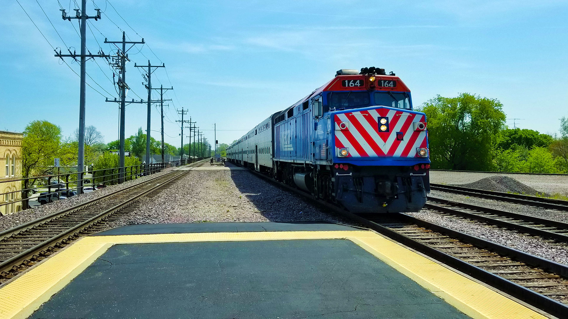 Blue train with red and white stripes on the front arrives at a station platform.