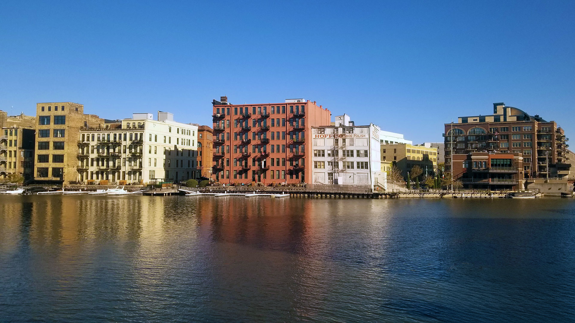 Different colored multi-story buildings along the river in Milwaukee.