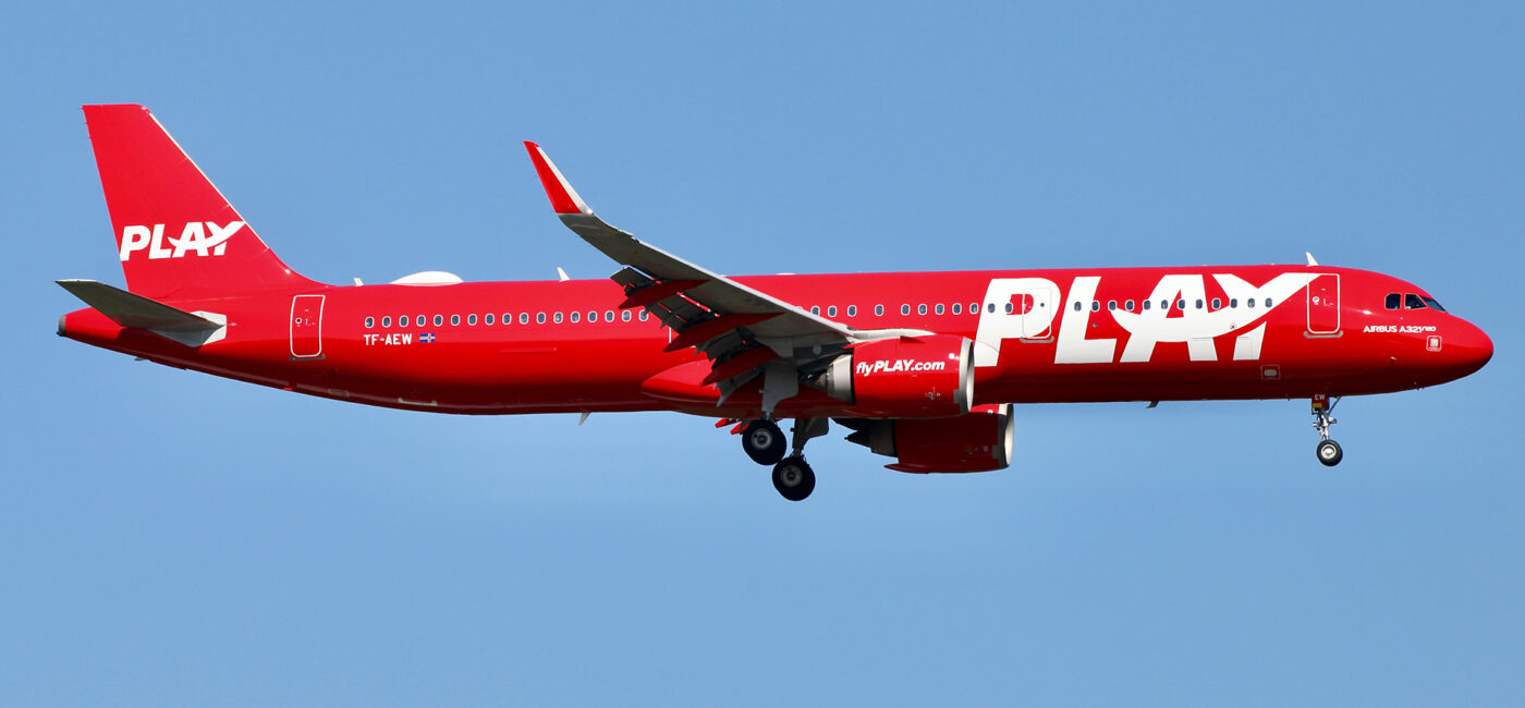 All red plane against blue sky landing at an airport.