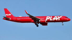 All red plane against blue sky landing at an airport.