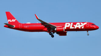 All red plane against blue sky landing at an airport.