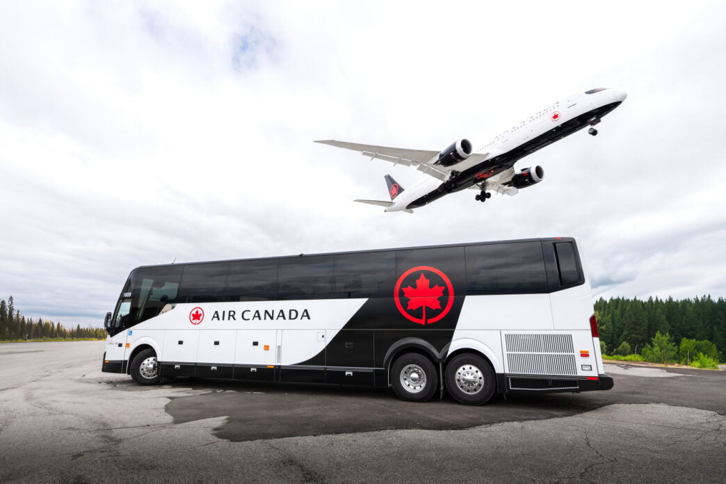 Air Canada bus in white and black livery with a Air Canada plane in white and black landing above the bus.