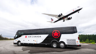 Air Canada bus in white and black livery with a Air Canada plane in white and black landing above the bus.