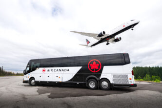 Air Canada bus in white and black livery with a Air Canada plane in white and black landing above the bus.