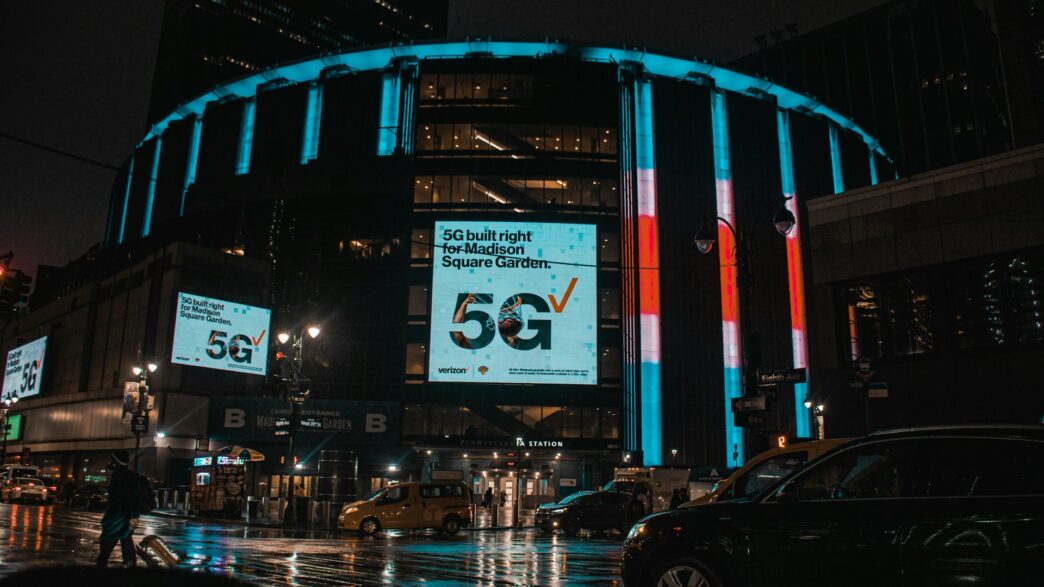 Madison Square Garden in New York City on a rainy night with neon signs shining brightly.