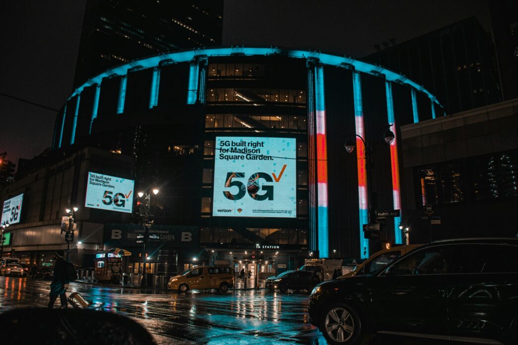 Madison Square Garden in New York City on a rainy night with neon signs shining brightly.