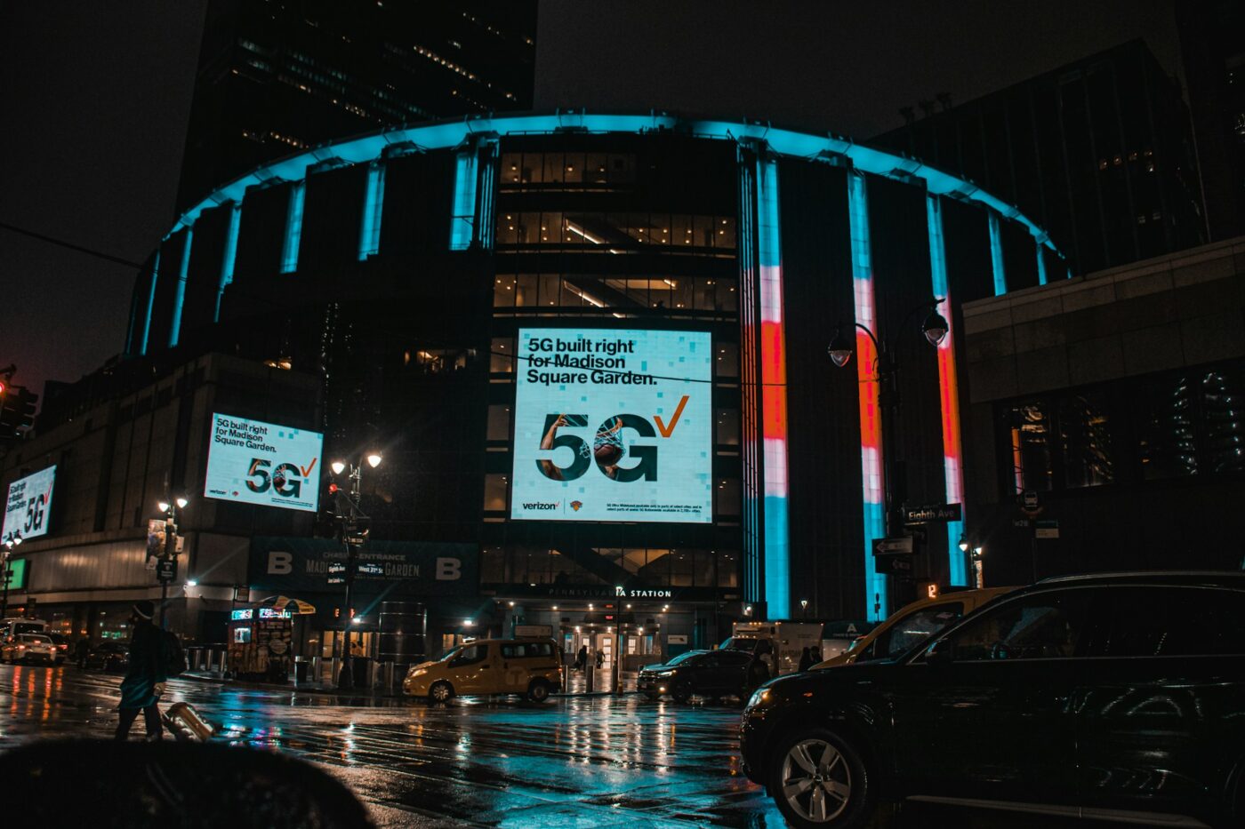 Madison Square Garden in New York City on a rainy night with neon signs shining brightly.