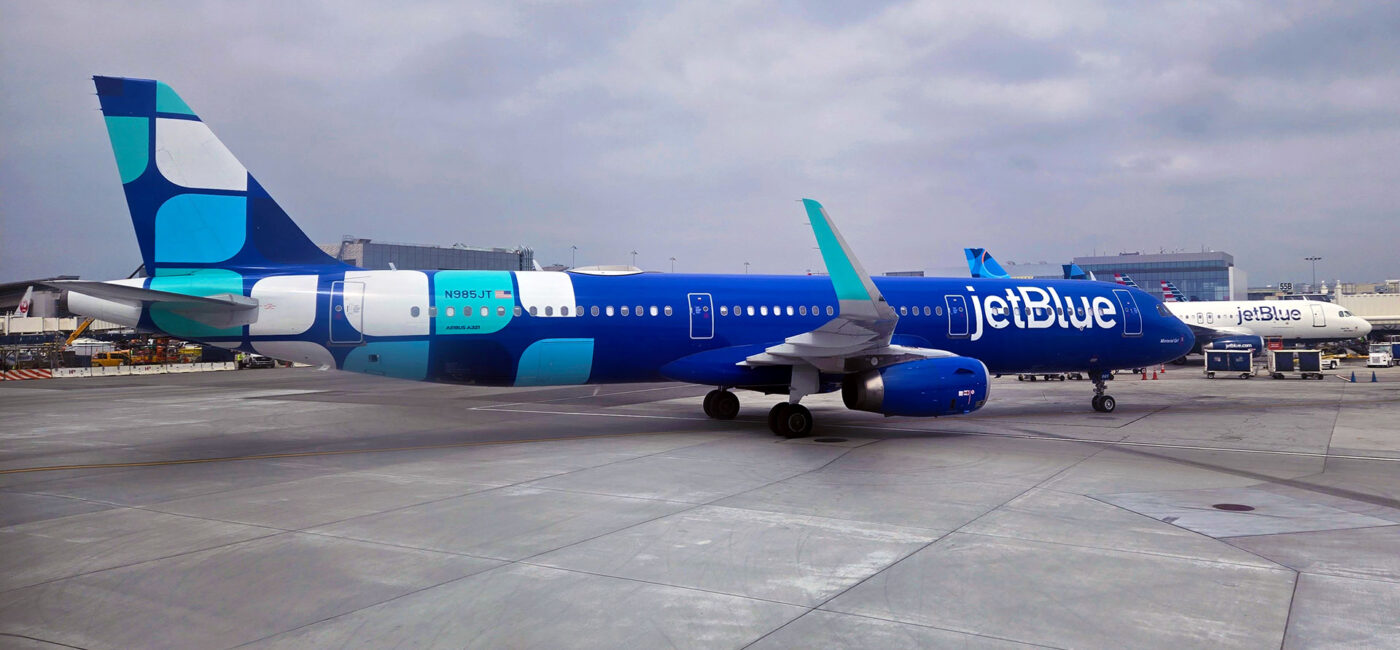 Blue jetBlue plane with a white and teal design livery at the gate in Los Angeles.