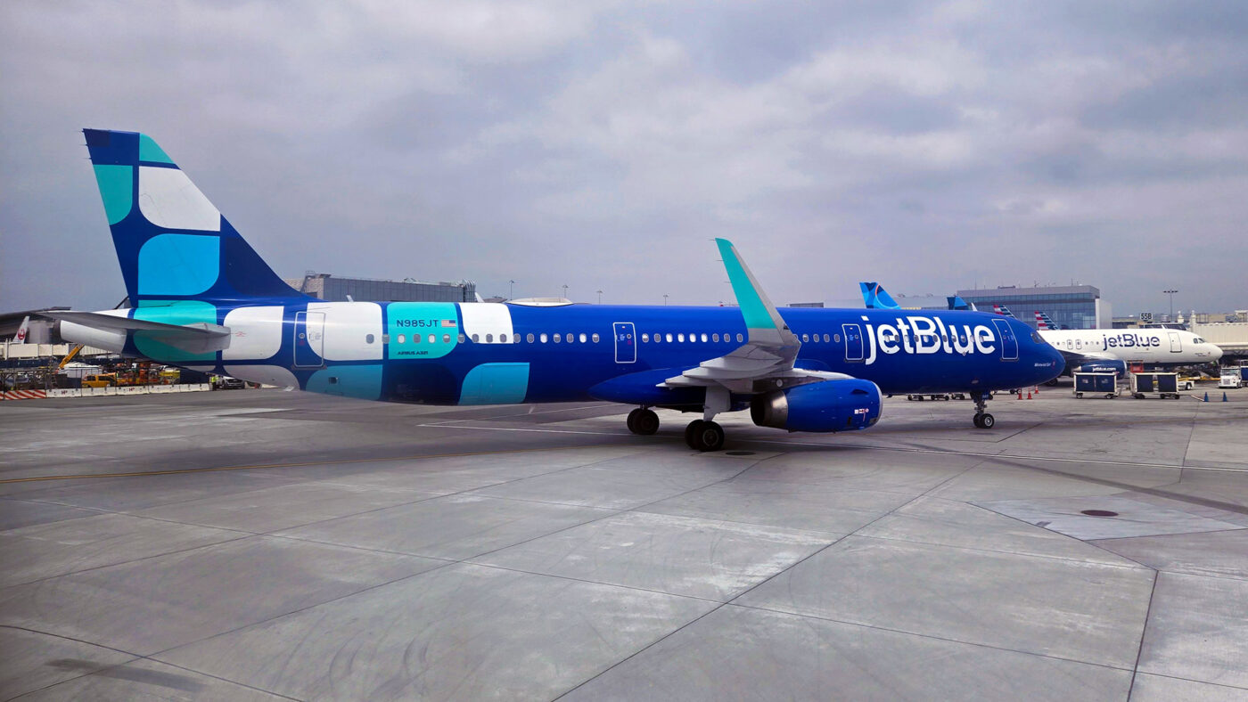 Blue jetBlue plane with a white and teal design livery at the gate in Los Angeles.