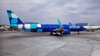Blue jetBlue plane with a white and teal design livery at the gate in Los Angeles.