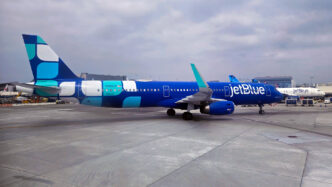 Blue jetBlue plane with a white and teal design livery at the gate in Los Angeles.